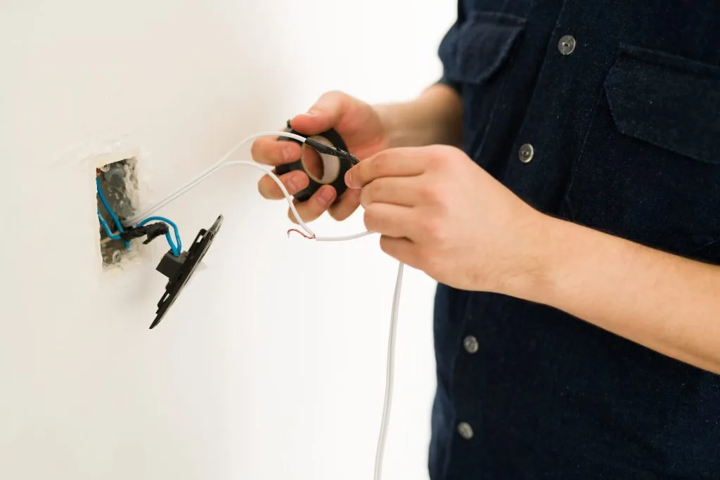 A person is connecting wires to an electrical outlet on a wall