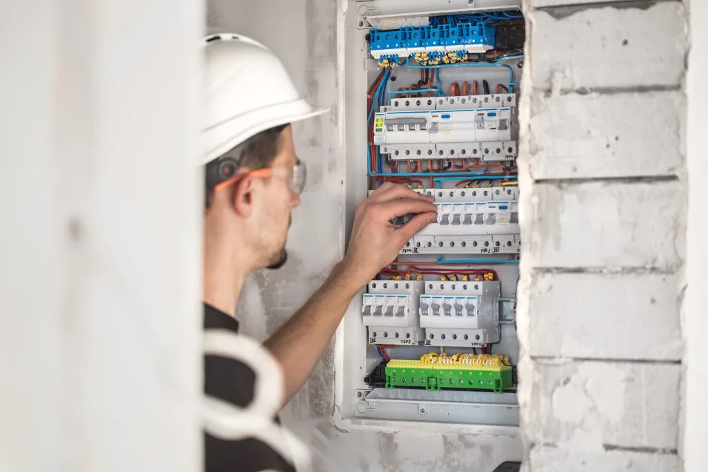 A worker adjusts electrical components within a partially finished wall
