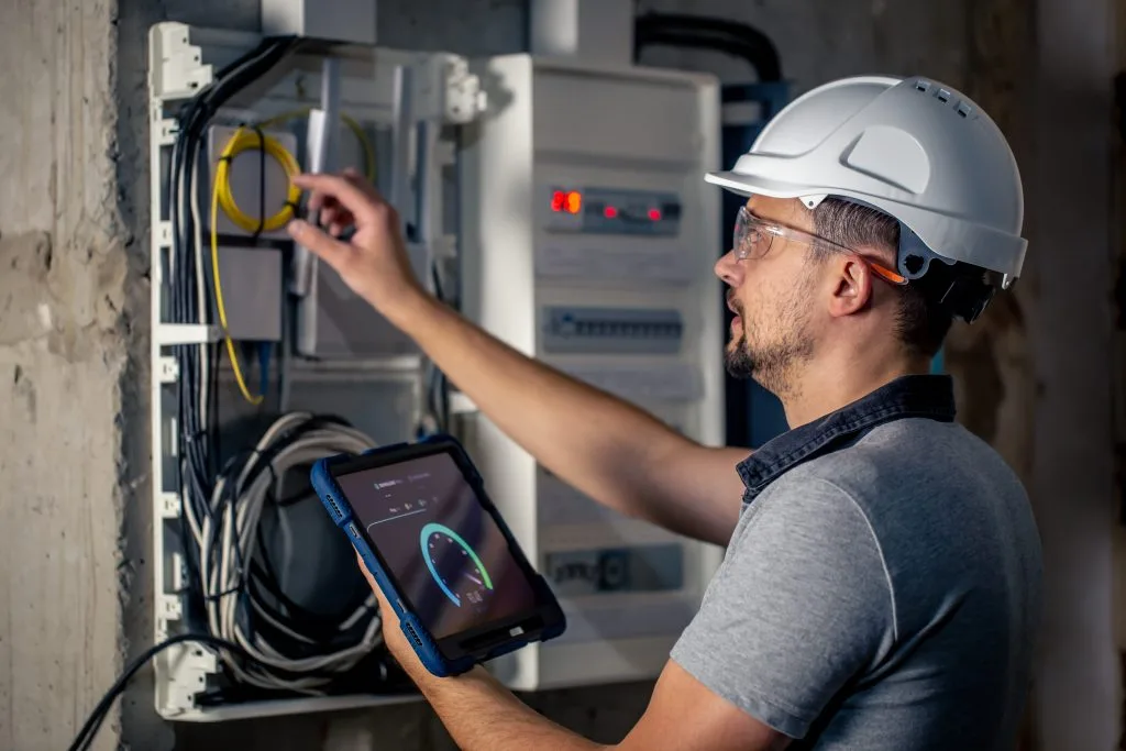 A technician inspects electrical connections while using a tablet for analysis