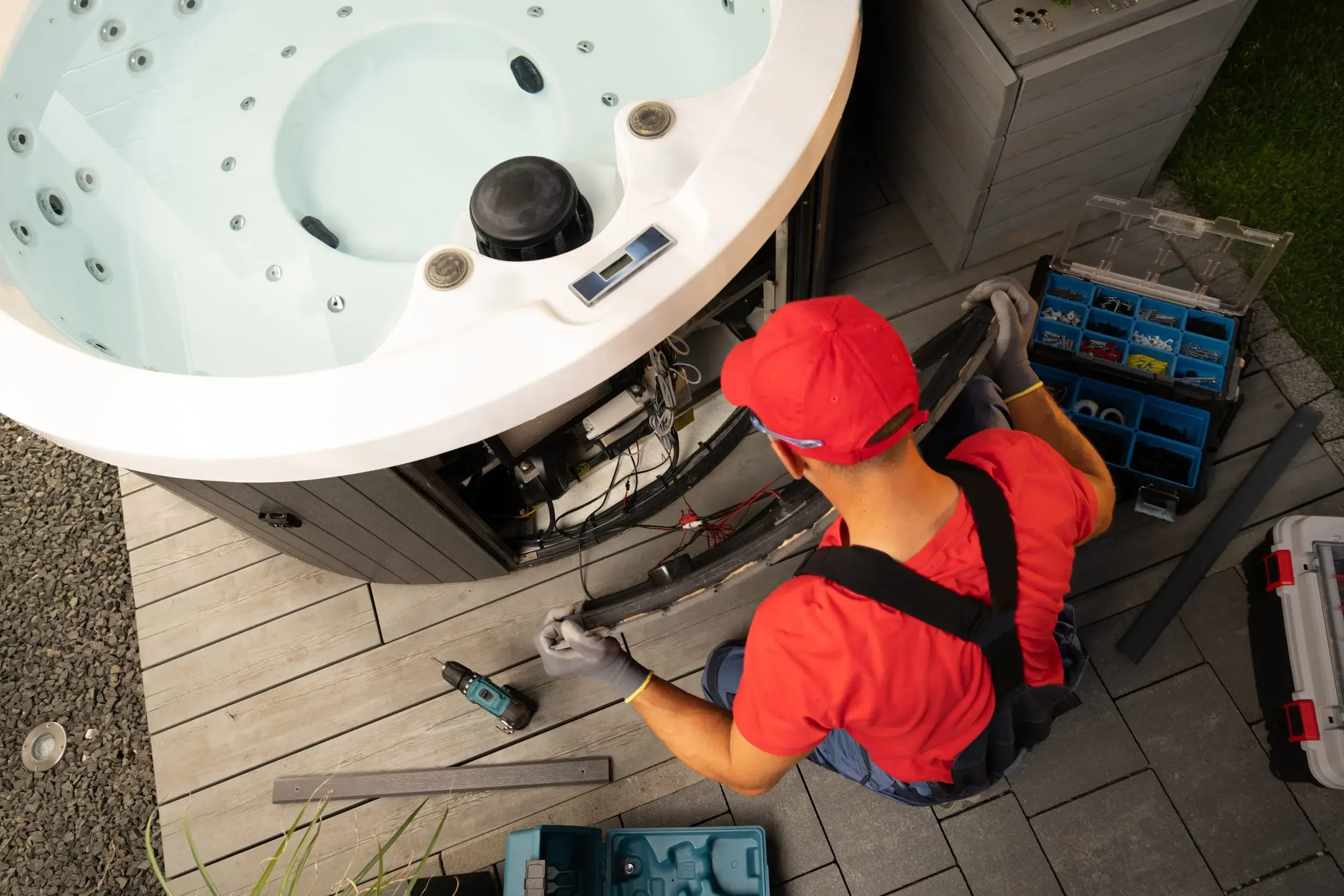 A person in a red shirt repairs equipment near a hot tub