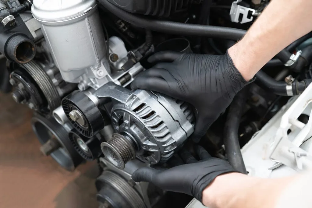 A person wearing gloves installs an alternator in a car engine